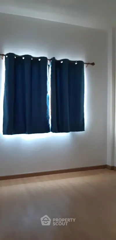 Spacious empty room with wooden flooring and dark curtains