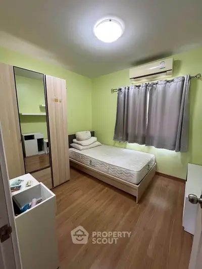 Cozy bedroom with wooden flooring and air conditioning, featuring a single bed and wardrobe.