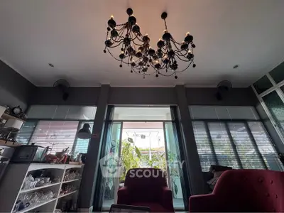Elegant living room with chandelier and large windows opening to a lush balcony view.