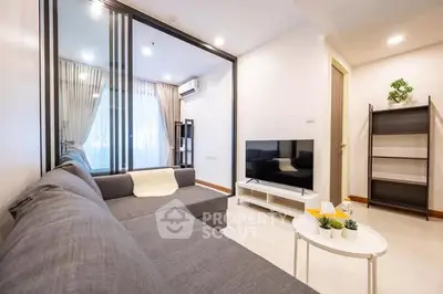 Modern living room with sleek gray sofa, flat-screen TV, and stylish decor in a bright, airy apartment.