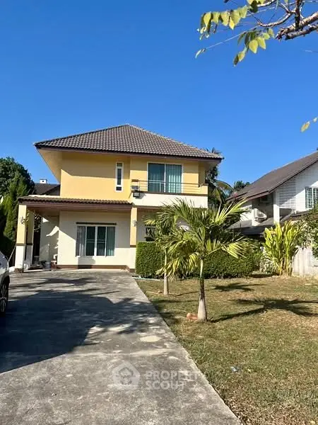 Charming two-story house with lush garden and spacious driveway under clear blue sky.