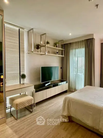 Modern bedroom with sleek decor and large TV, featuring natural light and stylish furnishings.