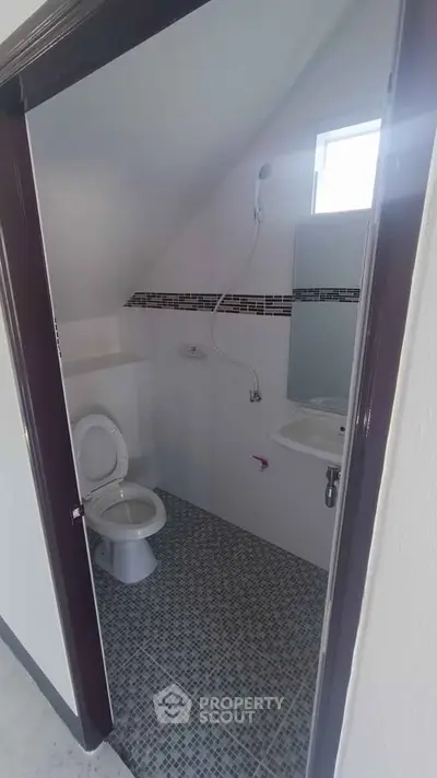 Compact bathroom with modern fixtures and tiled floor, featuring a toilet and sink under a sloped ceiling.