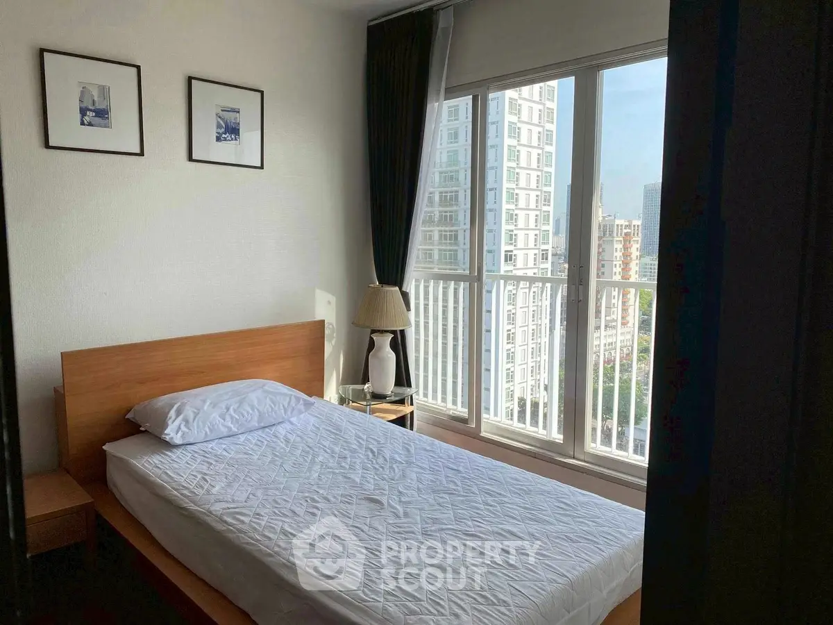 Cozy bedroom with large window offering city view, featuring a simple bed and elegant decor.