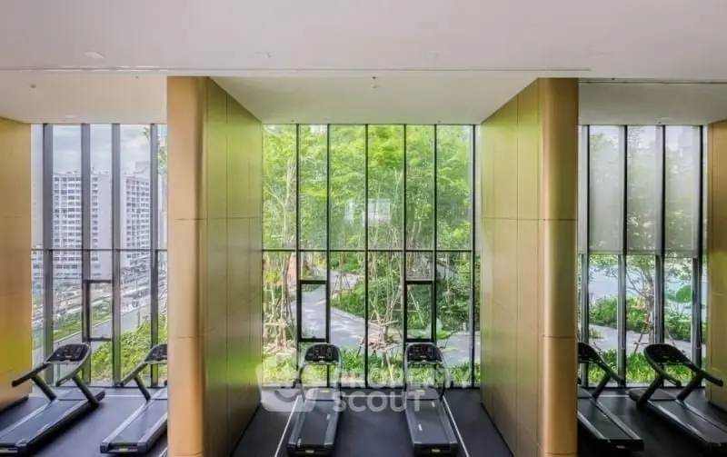 Modern gym with large windows offering a scenic view of lush greenery and cityscape, featuring state-of-the-art treadmills.