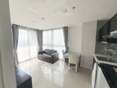 Bright modern living room with open kitchen, featuring large windows and sleek furnishings.