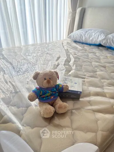 Cozy bedroom with plush teddy bear on a neatly made bed, inviting natural light through sheer curtains.