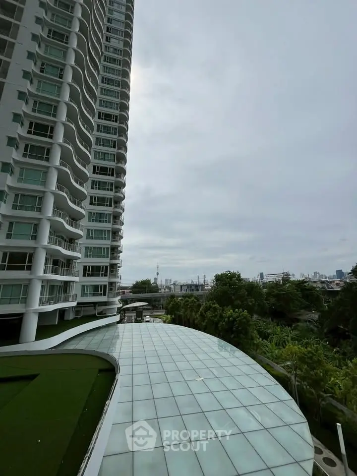 Modern high-rise building with expansive glass roof and lush greenery, offering a serene urban view.