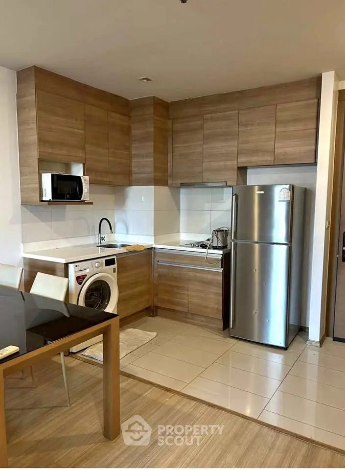 Modern kitchen with wooden cabinets, stainless steel fridge, and washing machine in sleek apartment.