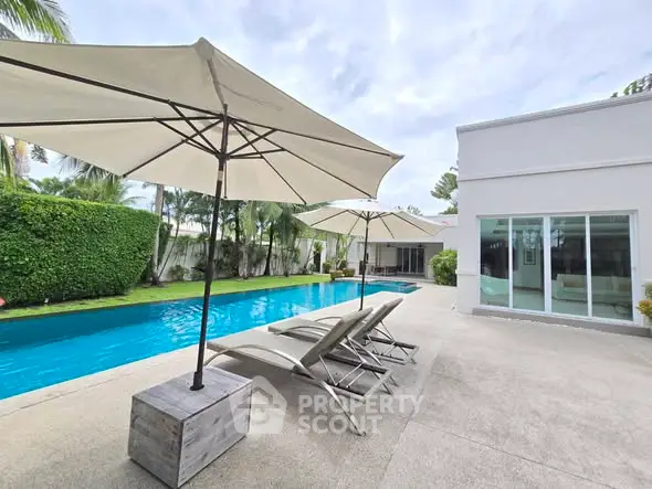 Luxurious poolside view with sun loungers and umbrellas in a modern villa setting.