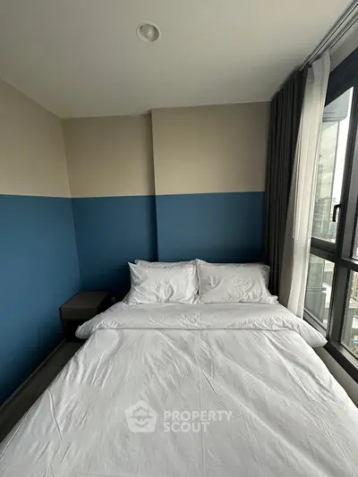 Modern bedroom with large window and stylish blue accent wall in urban apartment.
