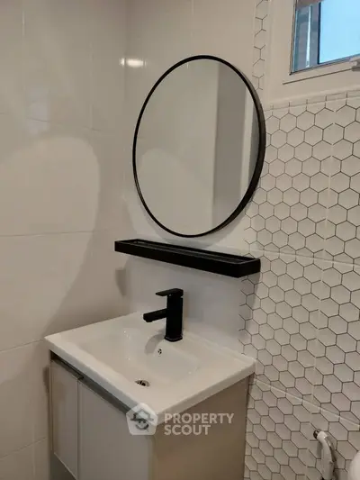 Modern bathroom with sleek sink, round mirror, and stylish hexagonal tiles.