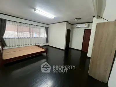 Spacious bedroom with dark wood flooring and large window, featuring air conditioning and ample natural light.
