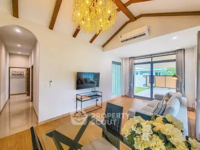 Luxurious living room with elegant chandelier and modern decor, featuring large windows and garden view.