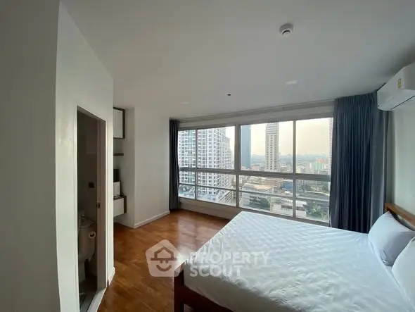 Spacious bedroom with city view and wooden flooring in modern apartment.