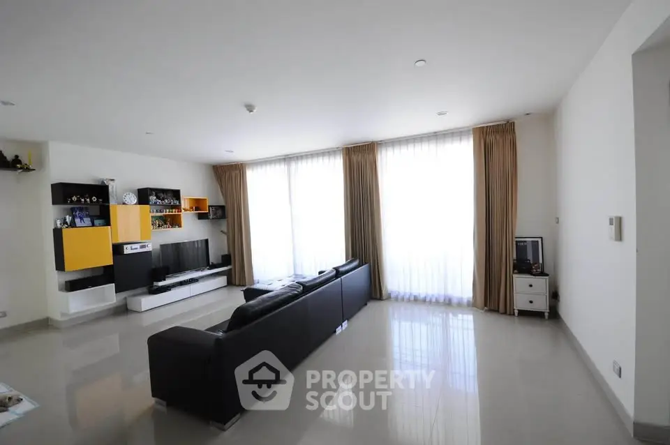 Spacious modern living room with sleek black sofa and large windows for natural light.