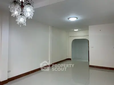 Spacious empty living room with elegant chandelier and glossy tiled flooring.