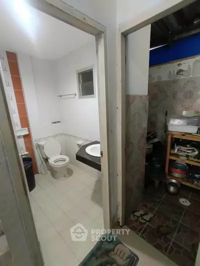 Compact bathroom with adjacent storage area, featuring basic fixtures and tiled flooring.