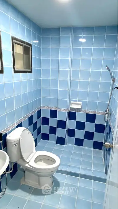 Modern blue-tiled bathroom with shower and toilet in real estate property.