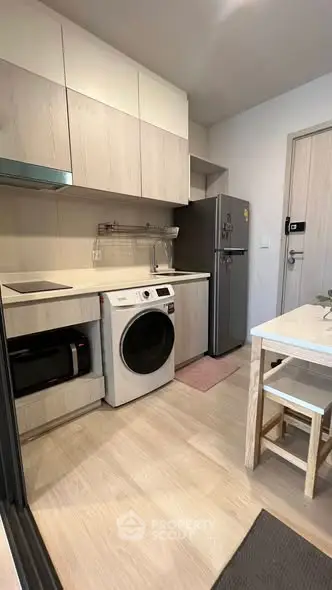 Modern kitchen with washing machine, fridge, and dining area in compact apartment.