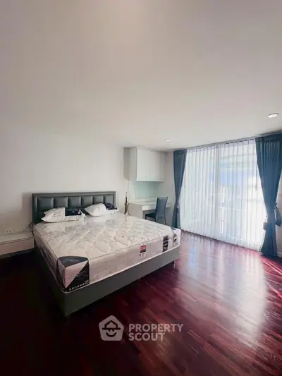 Spacious bedroom with elegant hardwood floors and large window for natural light.