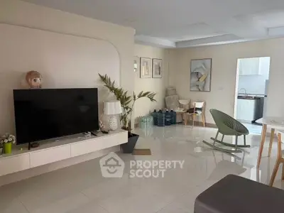 Spacious modern living room with sleek TV setup and stylish decor, leading to a bright kitchen area.