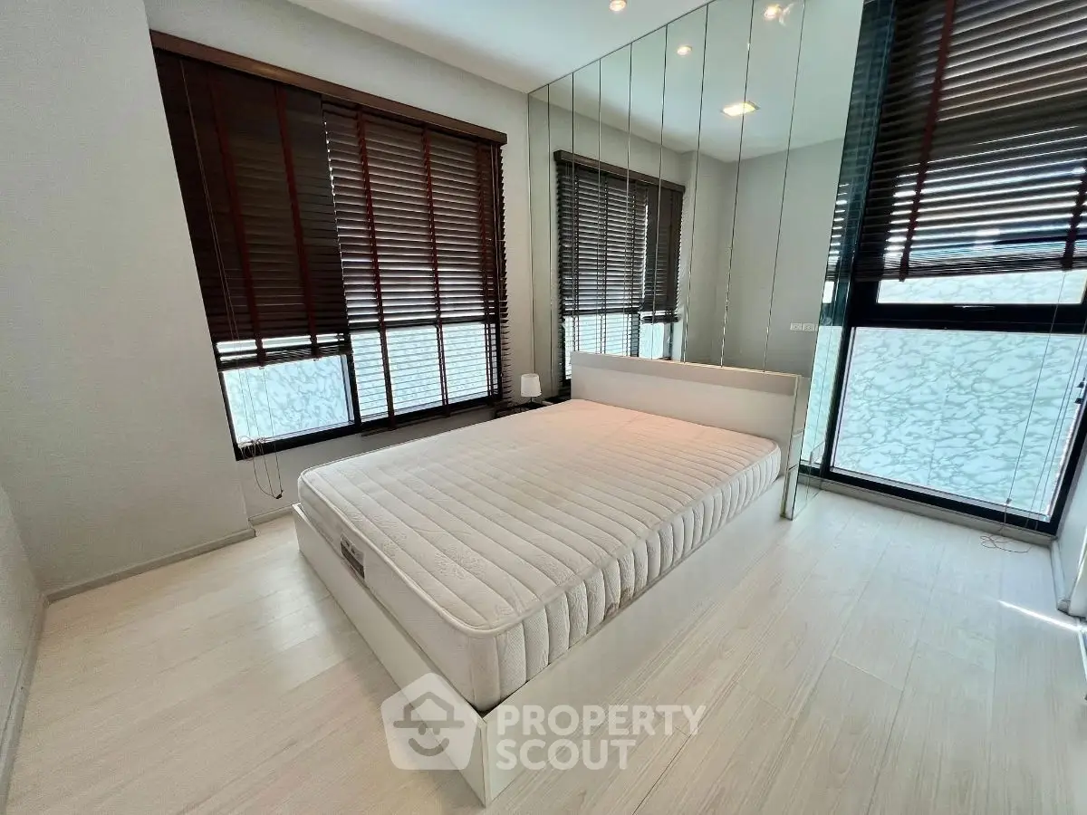 Modern bedroom with large windows and mirrored wall, featuring sleek design and natural light.