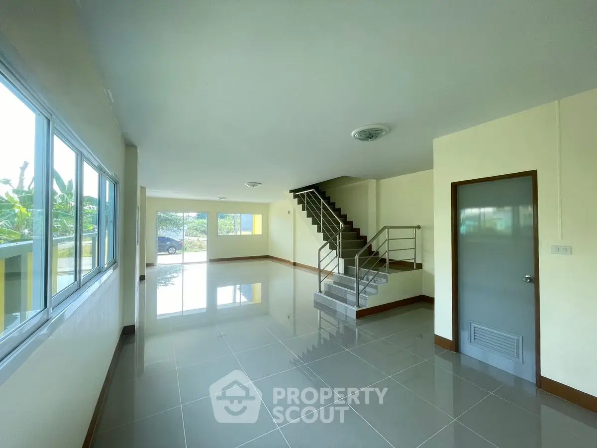 Spacious open-plan living area with modern staircase and large windows.