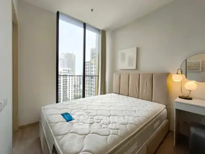 Modern bedroom with large window and city view, featuring a comfortable bed and stylish decor.