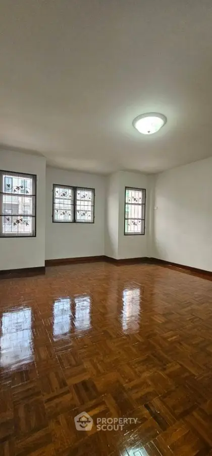 Spacious empty room with polished wooden floors and natural light from multiple windows.