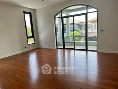 Spacious room with elegant wooden flooring and large windows offering natural light.