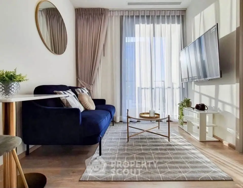 Modern living room with stylish decor, featuring a navy sofa, wall-mounted TV, and large window with sheer curtains.
