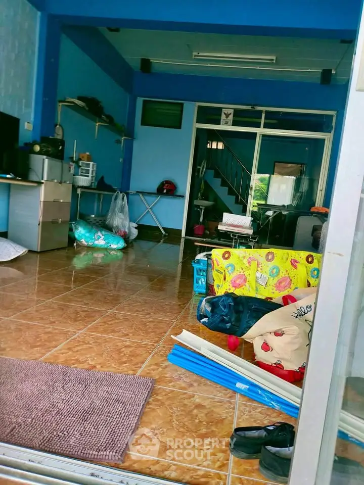 Spacious living area with tiled flooring and vibrant blue walls, featuring a staircase and ample natural light.