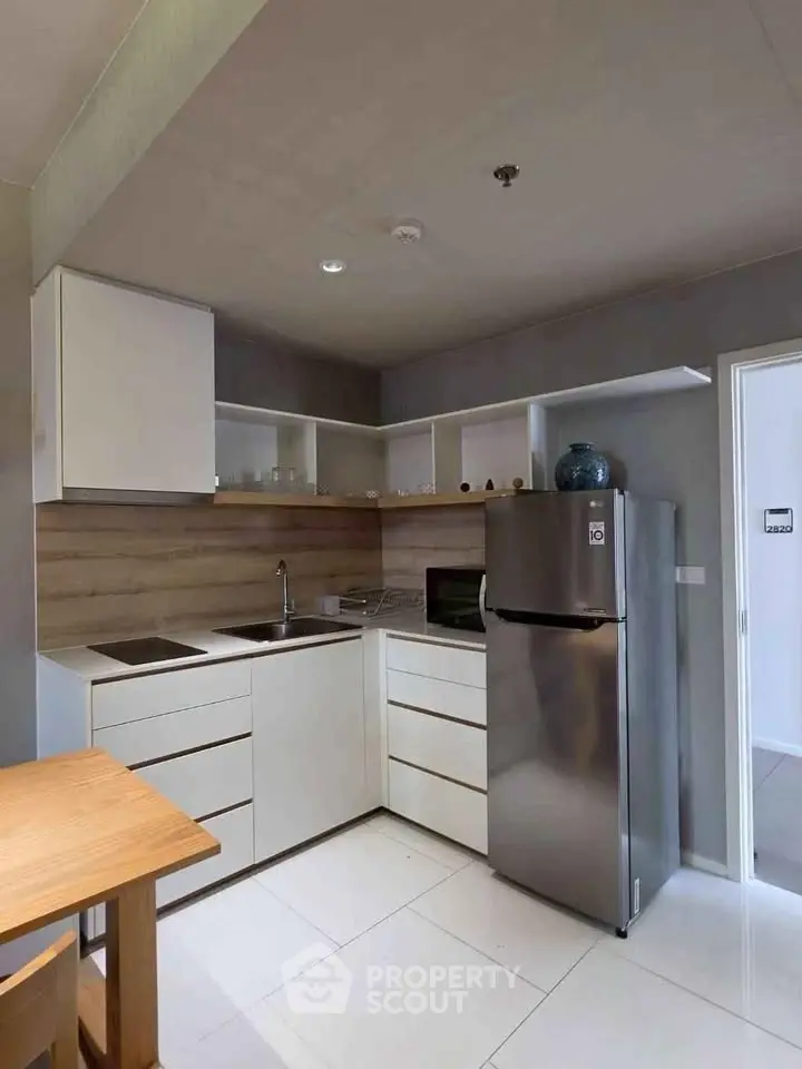 Modern kitchen with sleek white cabinets and stainless steel fridge in a compact layout.