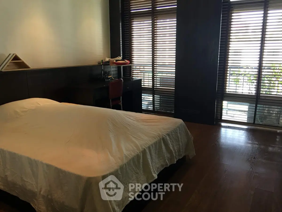 Spacious bedroom with wooden flooring and large windows offering natural light.