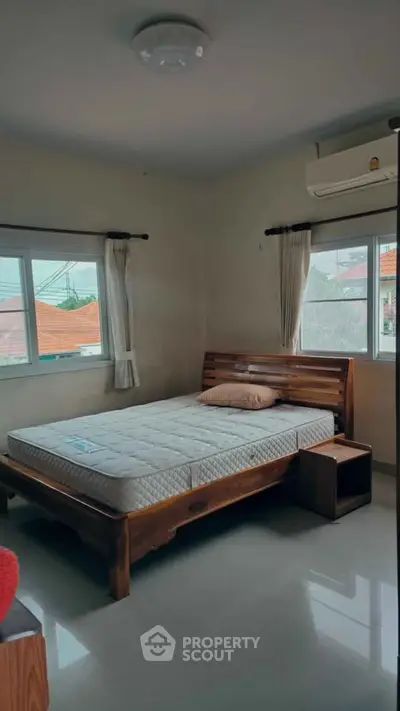 Cozy bedroom with wooden bed frame and large windows offering natural light.