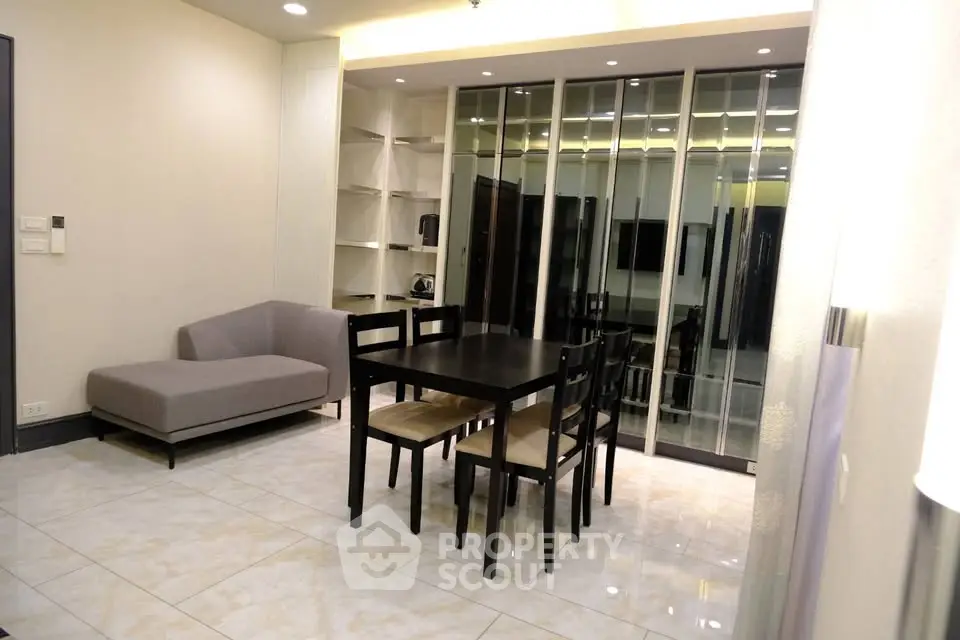 Modern dining area with sleek black table and mirrored wall in contemporary apartment.