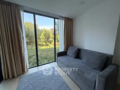 Cozy living room with large window and gray sofa overlooking lush greenery.