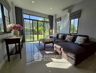 Bright living room with large windows and garden view, featuring a cozy sectional sofa and elegant decor.