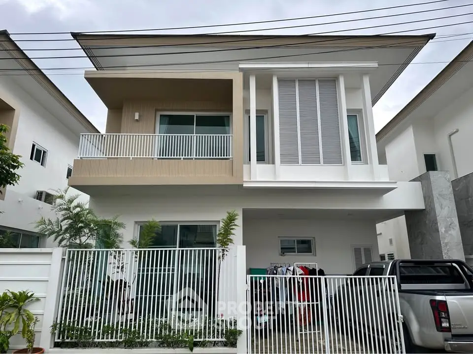Modern two-story house with balcony and gated driveway in suburban neighborhood.