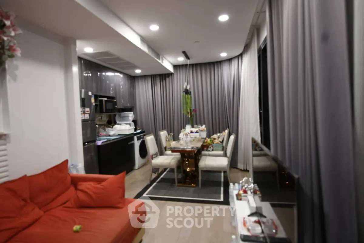 Modern living room with open kitchen, featuring sleek design and cozy seating area.