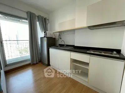 Modern kitchen with sleek cabinetry and city view from window, featuring compact appliances and wooden flooring.
