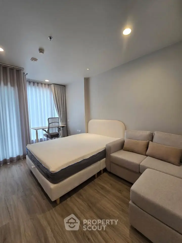 Modern bedroom with cozy bed, stylish sofa, and work desk in a bright, airy space.