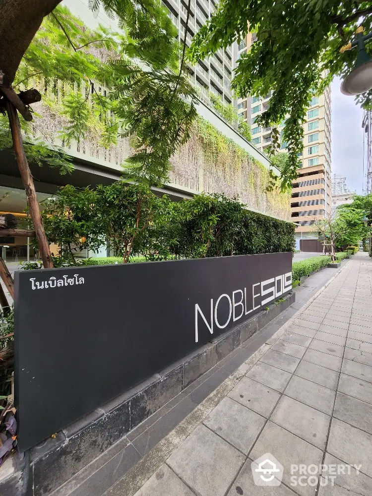 Modern urban building exterior with lush greenery and stylish signage on sidewalk.