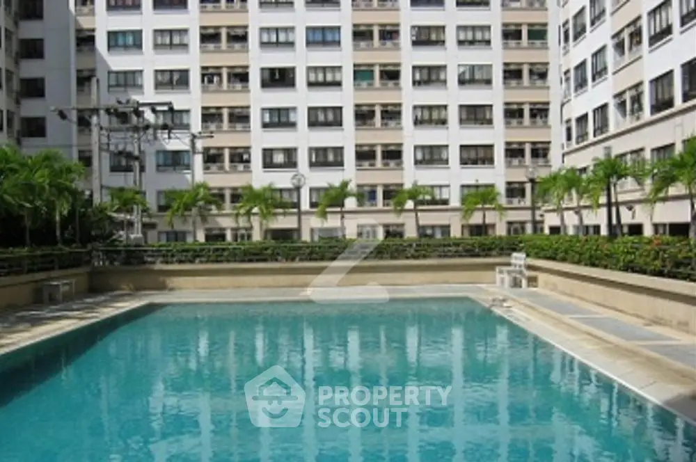 Inviting residential complex pool surrounded by lush greenery and a modern high-rise building, offering a tranquil urban oasis for relaxation and leisure.