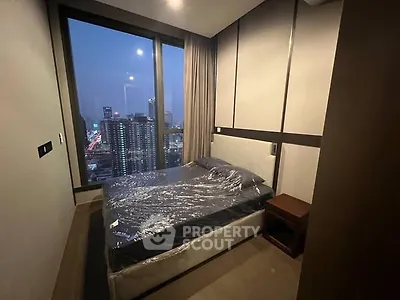 Modern bedroom with city view, featuring a cozy bed and large window.