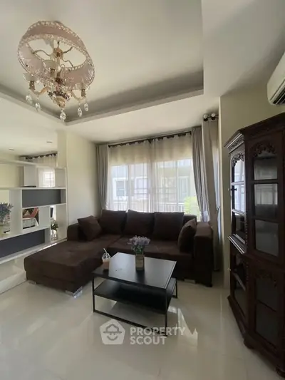Elegant living room with plush sofa, chandelier, and natural light through large windows.