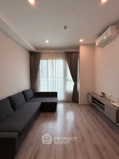 Modern living room with sleek design, featuring a dark sofa, wooden flooring, and large windows with curtains.