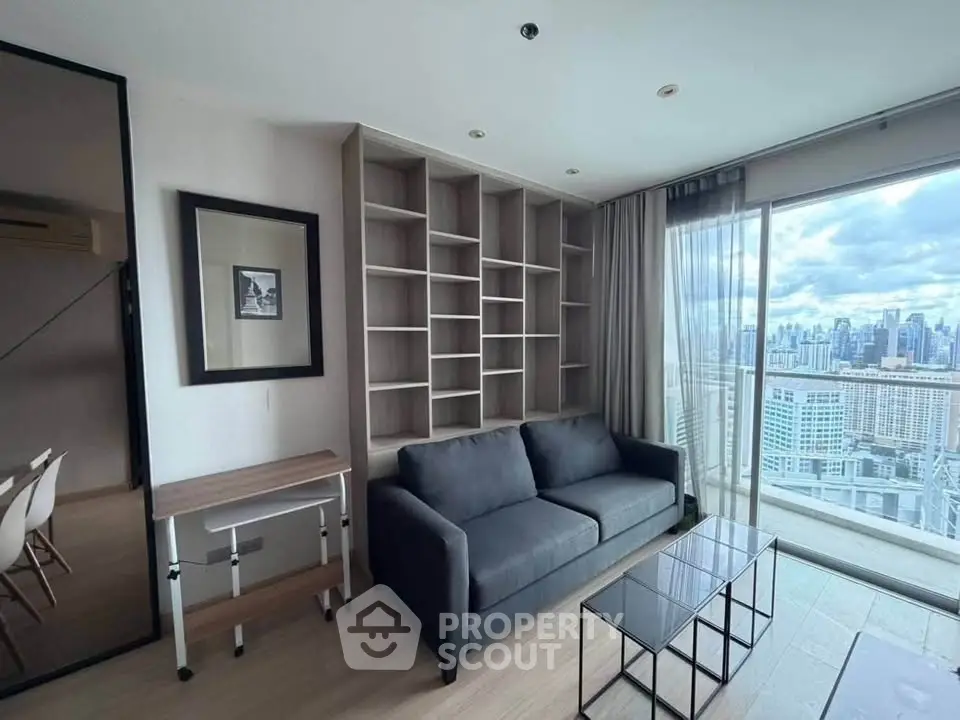 Modern living room with city view, featuring a sleek gray sofa and built-in shelving.