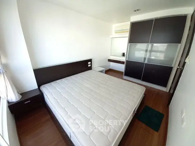 Spacious bedroom with large bed and modern dark wood wardrobe, featuring hardwood floors and ample natural light for a serene living space.